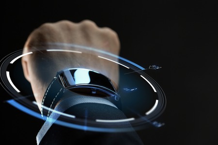 business, people and technology concept - close up of businessman hand with smartwatch and virtual projection over black backgroundの写真素材