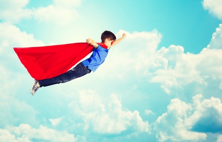 happiness, freedom, childhood, movement and people concept - boy in red superhero cape and mask flying in air over blue sky and clouds backgroundの写真素材