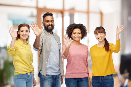 diversity, race, ethnicity and people concept - international group of happy smiling men and women waving hands over office backgroundの写真素材