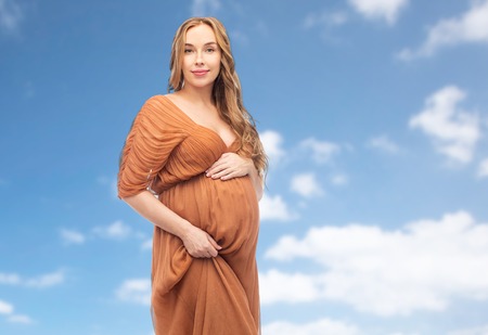 happy pregnant woman touching her belly over sky