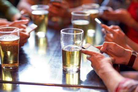 friends with beer and smartphones at bar or pubの写真素材