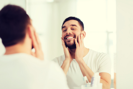happy young man looking to mirror at home bathroomの写真素材