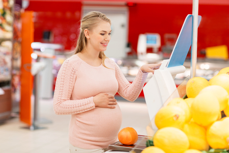 pregnant woman with grapefruit on scale at groceryの写真素材