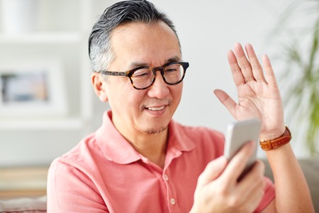 technology, people, lifestyle and communication concept - happy man with smartphone having video call at homeの写真素材