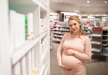 pregnancy, people, medicine, healthcare and beauty concept - happy smiling pregnant woman at pharmacy or cosmetics storeの写真素材