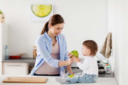 mother giving green apple to baby at home kitchenの写真素材