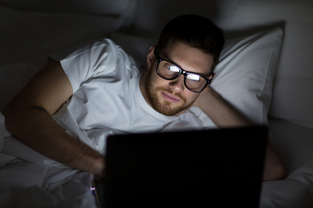 young man with laptop in bed at home bedroomの写真素材