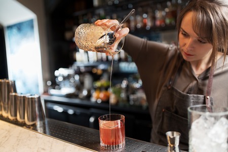 barmaid with glass and jug preparing cocktail