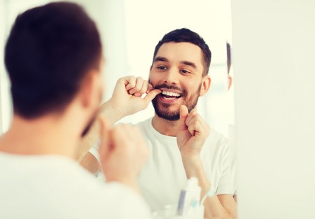 man with dental floss cleaning teeth at bathroomの写真素材