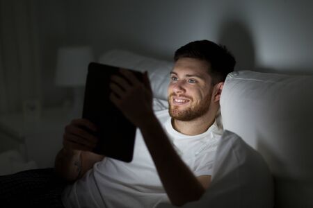 young man with tablet pc in bed at home bedroomの写真素材