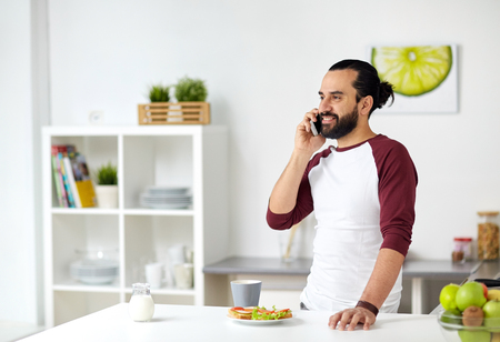 man calling on smartphone and eating at homeの写真素材