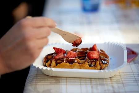 food, dessert and people concept - close up of woman eating waffle with strawberryの写真素材