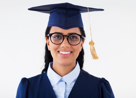 education, graduation and people concept - happy student woman in mortarboard and bachelor gown with...