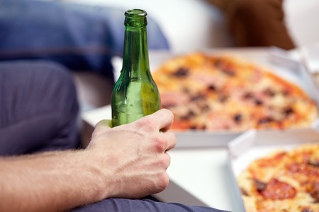 man with beer bottle and pizza at homeの写真素材