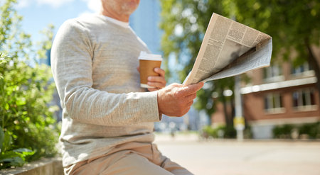 old age and people concept - senior man with coffee reading newspaper sitting on street bench