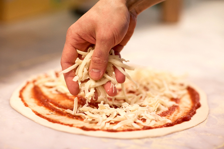 cook hand pouring cheese to pizza at pizzeriaの写真素材
