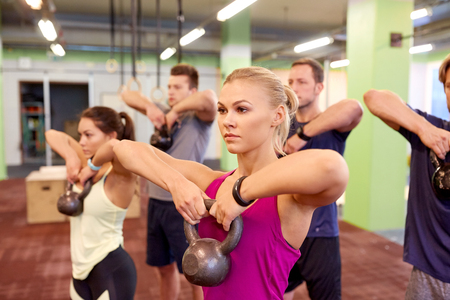 group of people with kettlebells exercising in gym
