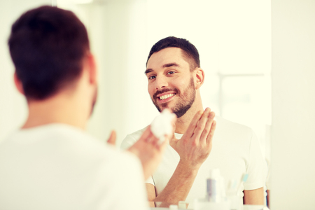 happy man applying shaving foam at bathroom mirrorの写真素材