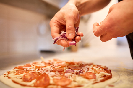 cook adding onion to salami pizza at pizzeriaの写真素材