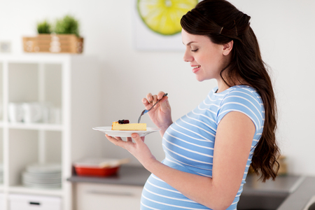 happy pregnant woman eating cake at home kitchenの写真素材