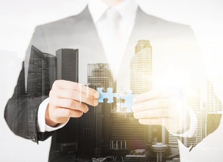 people, business and management concept - close up of businessman with puzzle pieces over city with double exposureの写真素材