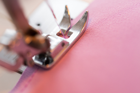 needlework and tailoring concept - sewing machine presser foot stitching fabric