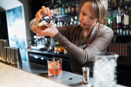 barmaid with glass and jug preparing cocktail