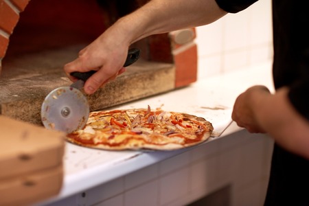cook hands cutting pizza to pieces at pizzeriaの写真素材