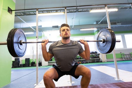 young man flexing muscles with barbell in gym