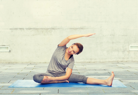 fitness, sport, people and healthy lifestyle concept - happy woman making yoga and stretching on mat over urban street backgroundの写真素材