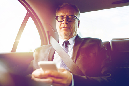 transport, business trip, technology and people concept - senior businessman texting on smartphone and driving on car back seatの写真素材