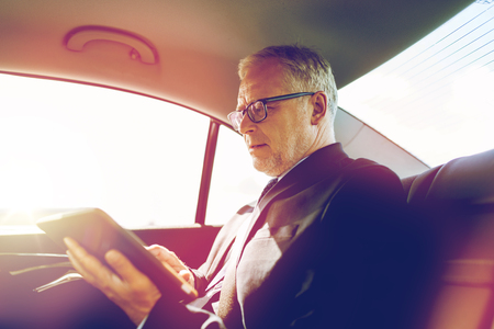 transport, business trip, technology and people concept - senior businessman with tablet pc computer driving on car back seatの写真素材