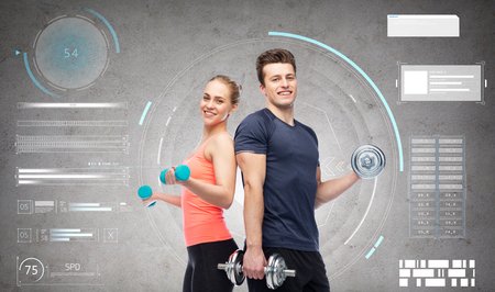 sport, fitness and people concept - happy sportive man and woman with dumbbells flexing muscles over gray backgroundの写真素材