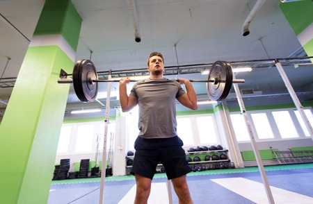 sport, fitness and people concept - smiling man doing exercise with barbell in gym