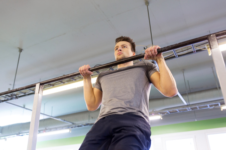 sport, fitness and people concept - man exercising and doing pull-ups on horizontal bar in gym