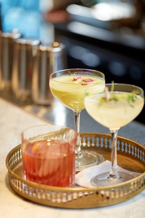 alcohol drinks and luxury concept - tray with glasses of cocktails at bar