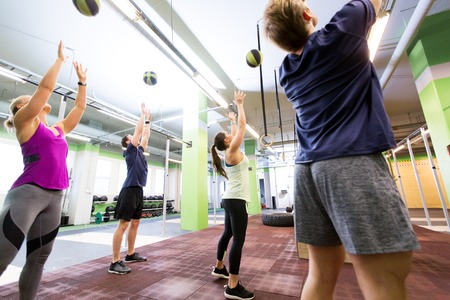 fitness, sport and exercising concept - group of people with medicine balls training in gym