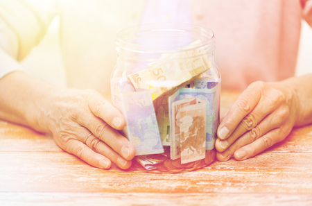 savings, money, annuity insurance, retirement and people concept - close up of senior woman hands with money in glass jarの写真素材