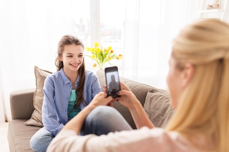 family, technology and people concept - happy mother and daughter with smartphone taking photo at homeの写真素材
