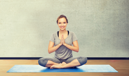 fitness, sport, people and healthy lifestyle concept - woman making yoga meditation in lotus pose on mat over gym room backgroundの写真素材