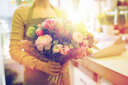 people, business, sale and floristry concept - close up of florist woman holding bunch at flower shopの写真素材