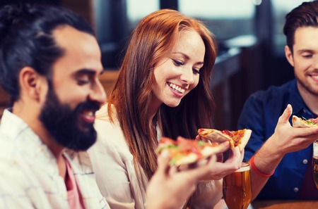 leisure, food and drinks, people and holidays concept - smiling friends eating pizza and drinking beer at restaurant or pubの写真素材