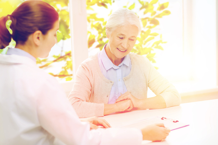 medicine, age, health care and people concept - doctor with clipboard and senior woman meeting at hospitalの写真素材