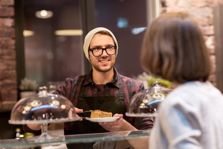 man or barman with cakes serving customer at cafeの写真素材