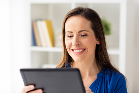business, people and technology concept - happy smiling woman in glasses with tablet pc computer working at home or officeの写真素材