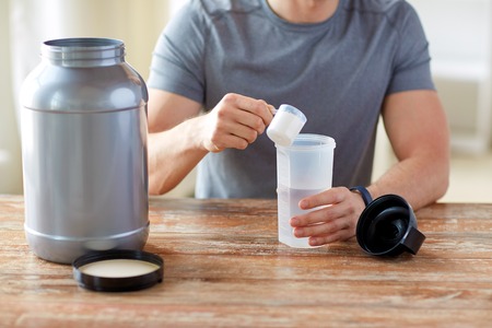 sport, healthy lifestyle and people concept - close up of man wearing fitness tracker with jar and bottle preparing protein shakeの写真素材