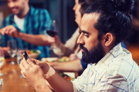 man with smartphone and friends at restaurantの写真素材