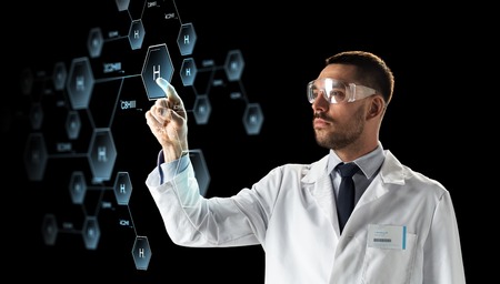 science, chemistry and people concept - male doctor or scientist in white coat and safety glasses touching virtual projection of chemical formula over black backgroundの写真素材