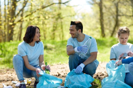volunteering, charity, people and ecology concept - group of happy volunteers with garbage bags...