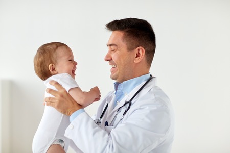 medicine, healthcare, pediatry and people concept - happy doctor or pediatrician holding baby on medical exam at clinicの写真素材